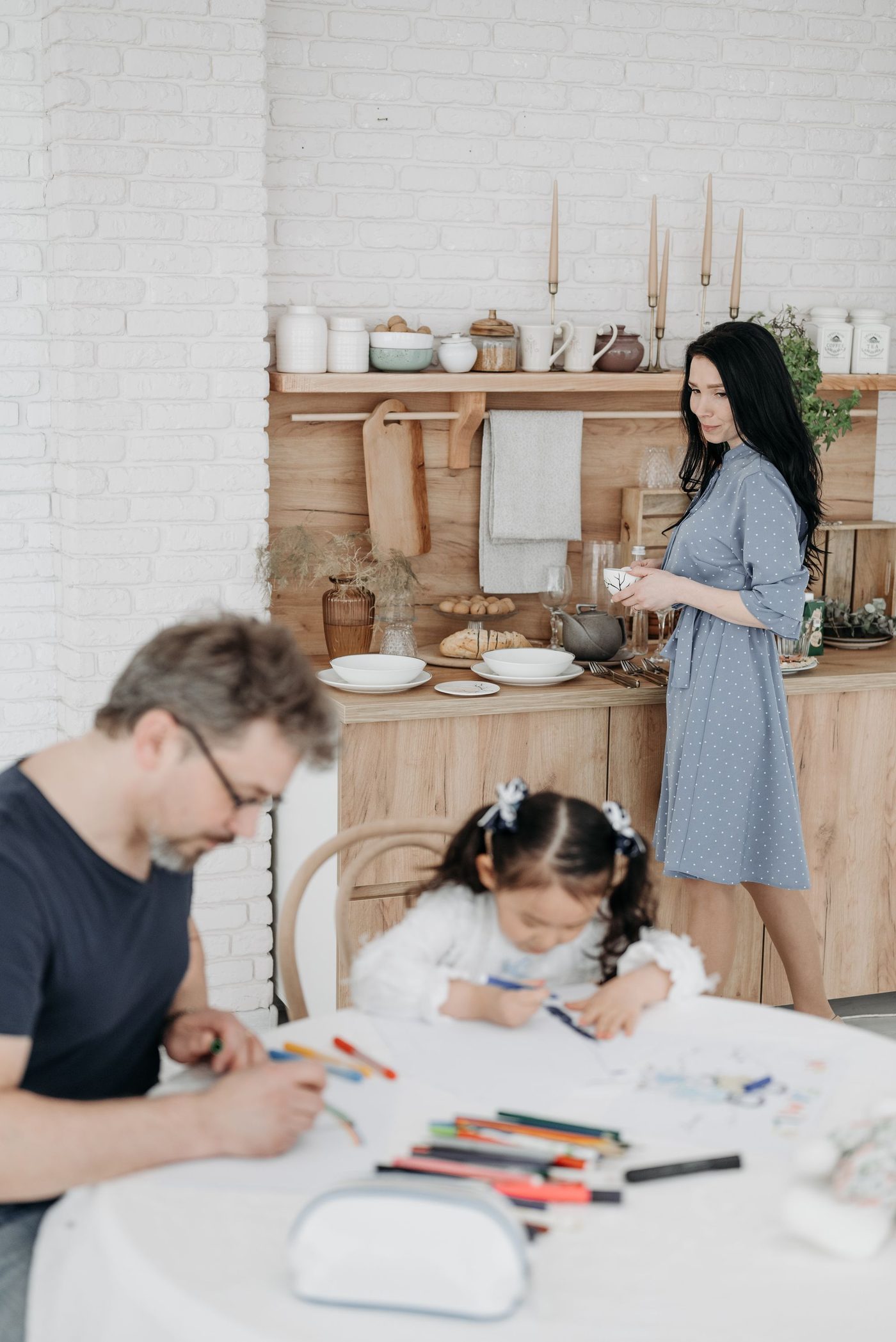 A father and daughter drawing together at the kitchen table while her mother cooks