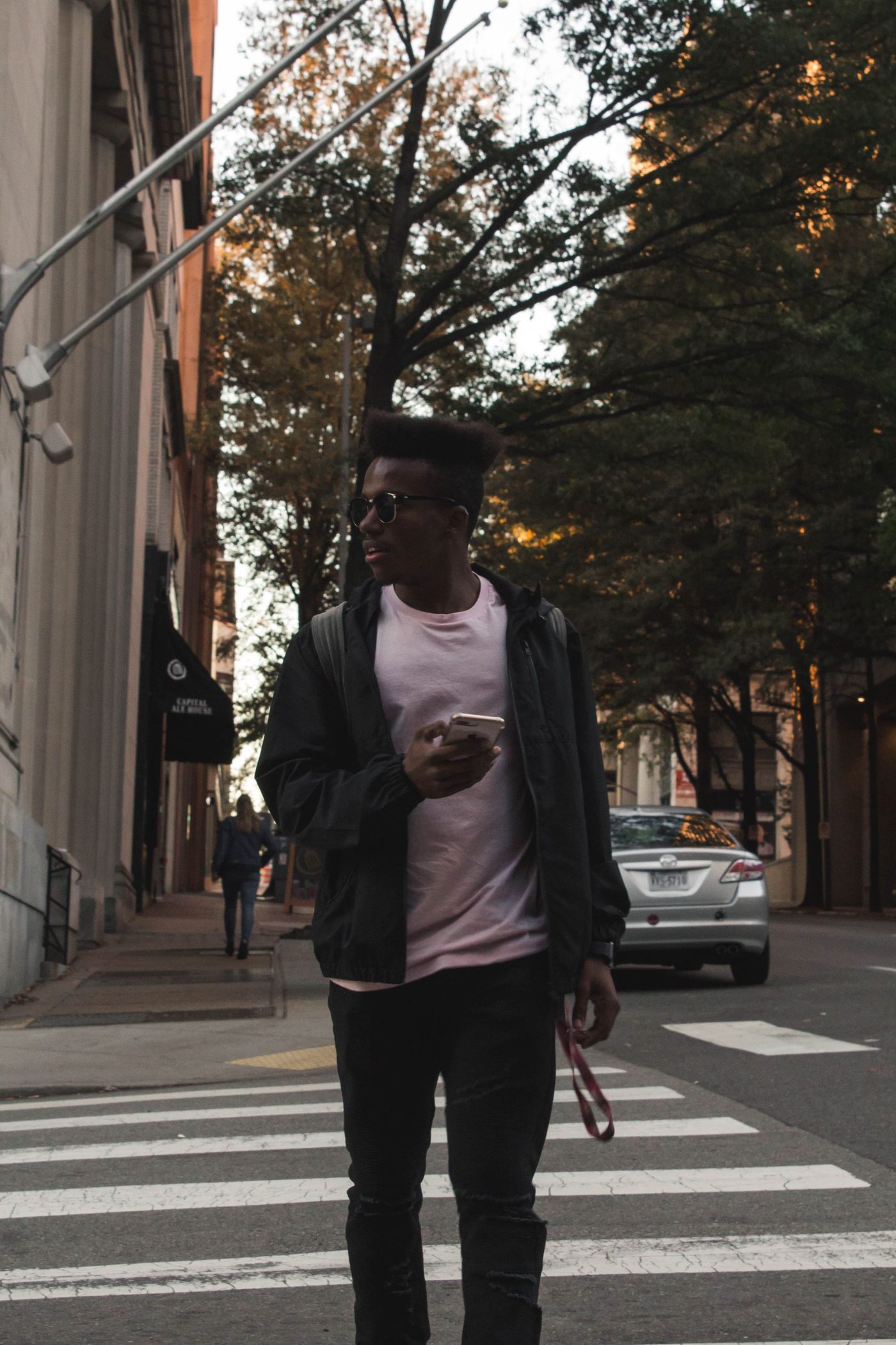 A man in a jacket crossing a city street, phone in hand